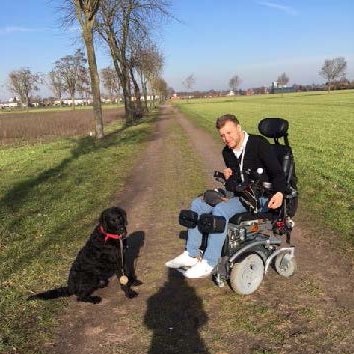 Assitenzhund apportiert einen Ball auf einem Feldweg, Christian sitzt im elektrischen Rollstuhl
